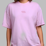 Person wearing a light pink t-shirt with a logo on a plain background